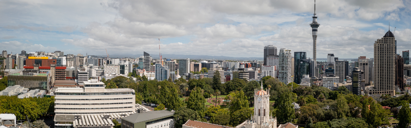 A cityscape with many skyscrapers and trees. There is one very tall and thin building that stands above the rest. 